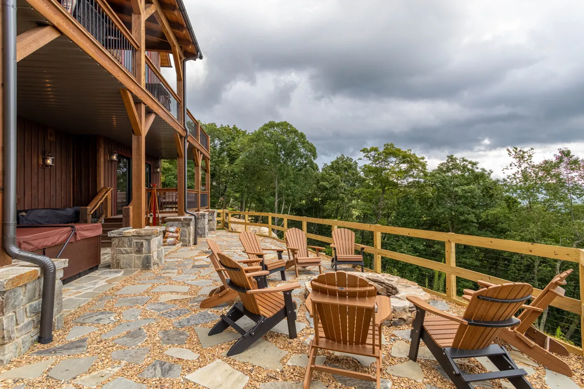An inviting stone patio with wooden chairs and outdoor furniture surrounded by trees, perfect for gathering around the fire pit, socializing, or enjoying the peaceful outdoors just steps from the indoor fun.