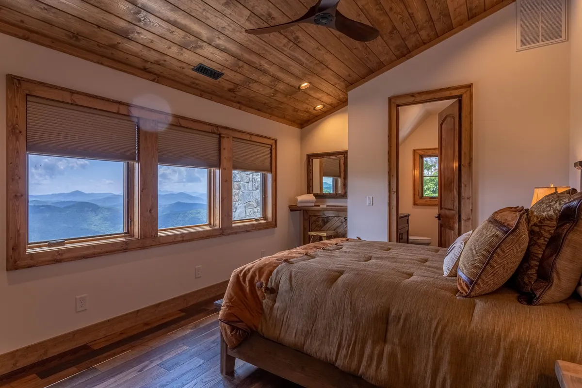 A serene bedroom featuring textured bedding, expansive windows that frame breathtaking mountain vistas, and warm wooden ceilings and furniture, creating a peaceful, inviting space ideal for relaxation and a peaceful night's sleep.