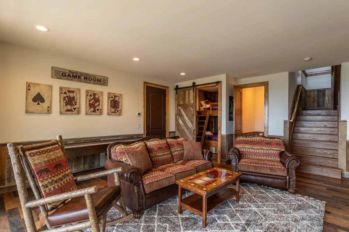 A cozy game room featuring a sofa set, coffee table, and stairs leading up. The space is marked by a prominent 'game room' sign and is inviting, clearly designed for socializing, playing board games, and family gatherings.
