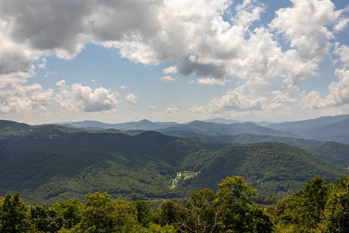 A sweeping view of lush green valleys and layered mountain ranges under a dramatic sky, capturing the natural grandeur and adventure potential of the surrounding landscape. The scene evokes possibilities for hiking, nature photography, and outdoor exploration, perfectly aligned with Eagles Nest's adventure-focused amenities.