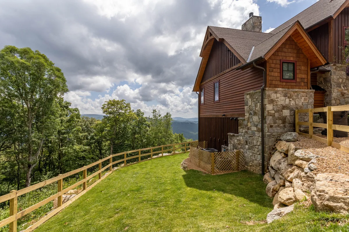 This image showcases the beautiful stone and wooden structure of Majestic View Hideaway, surrounded by an expansive green lawn and mature trees. The backdrop features sweeping mountain vistas, providing the perfect scenic setting for outdoor relaxation or memorable group photos. The serene, welcoming atmosphere is ideal for multi-generational gatherings.