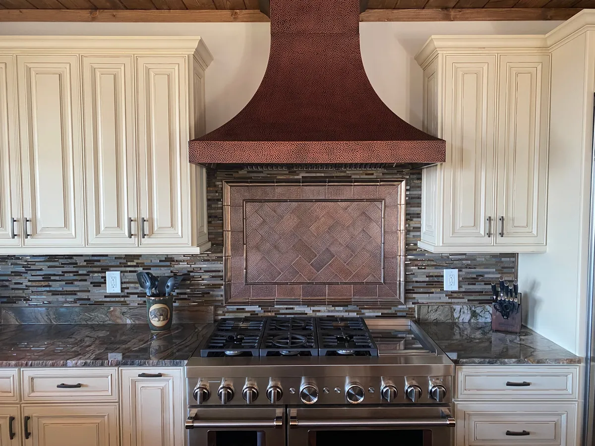 An inviting view of the gourmet kitchen, showcasing a copper hood, marble countertops, decorative backsplash, and stainless steel appliances. The setting is ideal for preparing and serving a feast, with an ambiance suited to entertaining and culinary creativity.