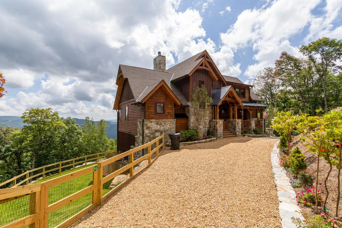 This image features the home's stone facade, wooden accents, landscaped entrance, and a driveway leading up to the front door. The inviting porch and surrounding greenery evoke the feeling of arrival and outdoor connection, making it clear that the property is well integrated into its natural surroundings.