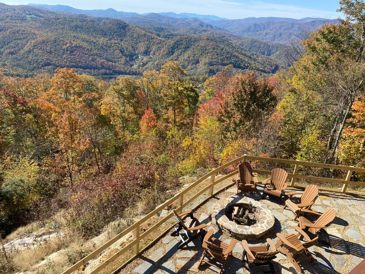 A cozy fire pit encircled by Adirondack chairs, with a dramatic mountain backdrop and autumn foliage. The scene invites guests to unwind by the fire after a day of exploration, enjoying sunset views and the tranquil beauty of Eagles Nest.