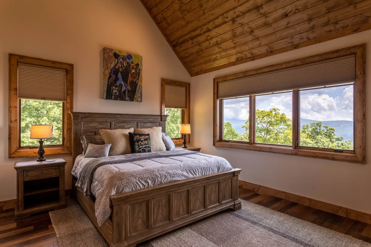 A tranquil bedroom with a plush bed positioned near large windows, letting in natural light and offering glimpses of the scenic outdoors. Subtle artwork and a tidy nightstand add to the sense of serenity, making the space feel like a restful sanctuary.