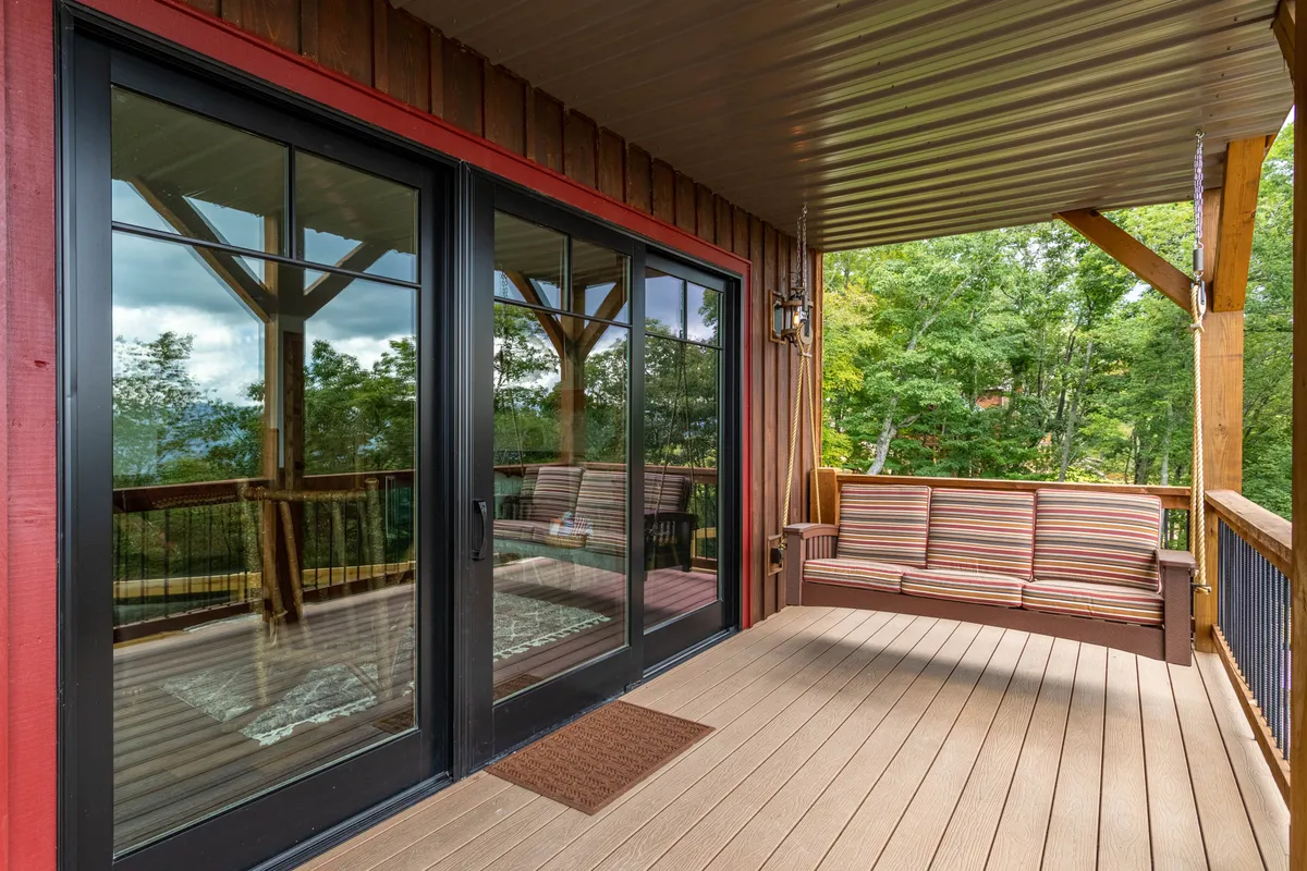 This exterior image features large glass sliding doors opening onto a deck with a striped couch and wooden railing. The setting offers serene mountain views—perfect for sipping wine or enjoying a relaxing moment after local culinary adventures.
