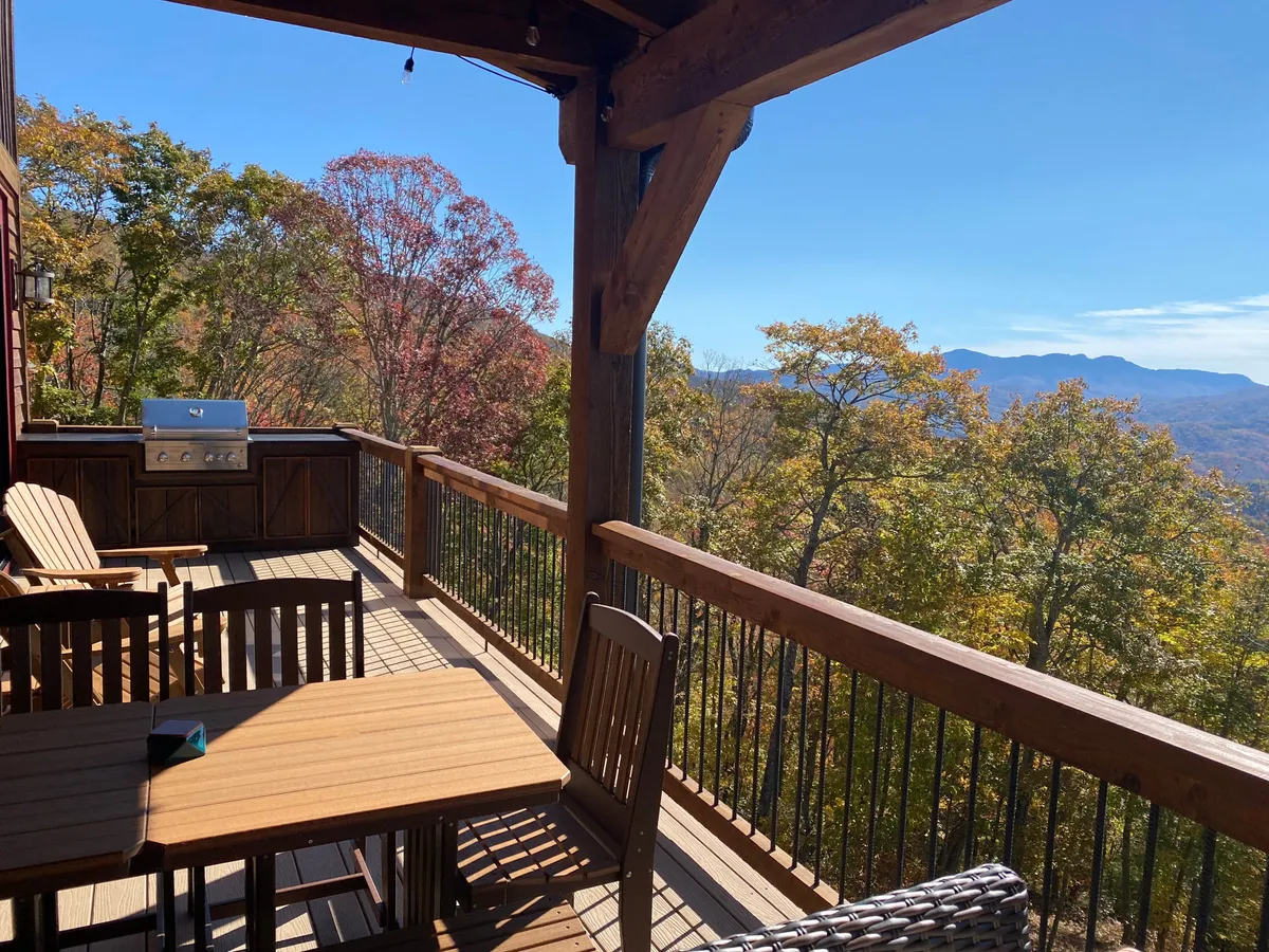 A tranquil outdoor dining area with wooden chairs and a grill sits before a sweeping mountain view. The setting invites guests to dine, relax, and soak in the Blue Ridge Mountains after a day of outdoor activity.