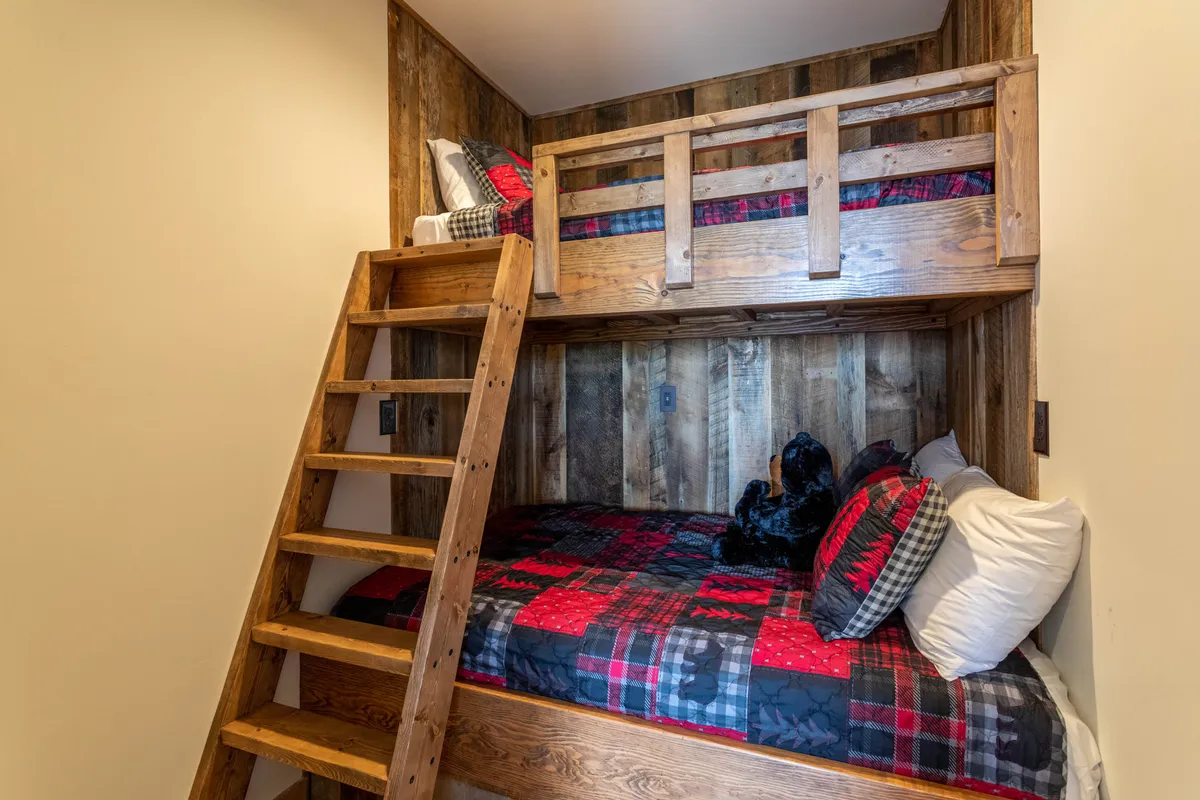 A playful bedroom with wooden bunk beds, plaid bedding, and a sturdy wooden ladder—ideal for children or family groups. The space feels warm, fun, and welcoming, perfect for late-night chats and cozy blanket forts.